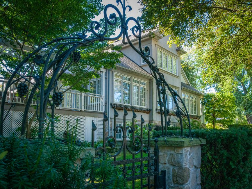 A charming house is visible through a beautifully designed wrought iron gate, surrounded by lush greenery.