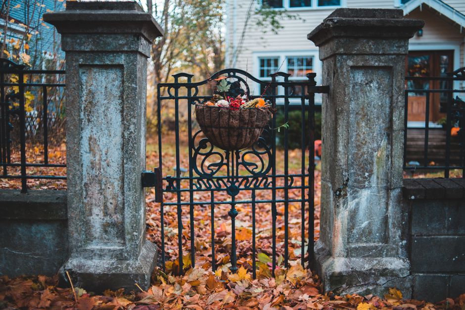 Stone gate adorned with autumn decorations, framed by fall foliage, leading to a traditional home.